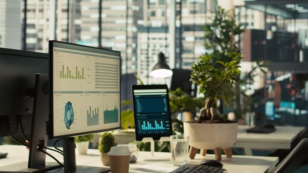 Biurko w biurze z monitorem i tabletem wyświetlającymi wykresy i dashboardy analityczne